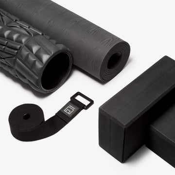 group shot of gray rolled up yoga mat, textured black foam roller, d-ring yoga strap and two black foam yoga blocks.