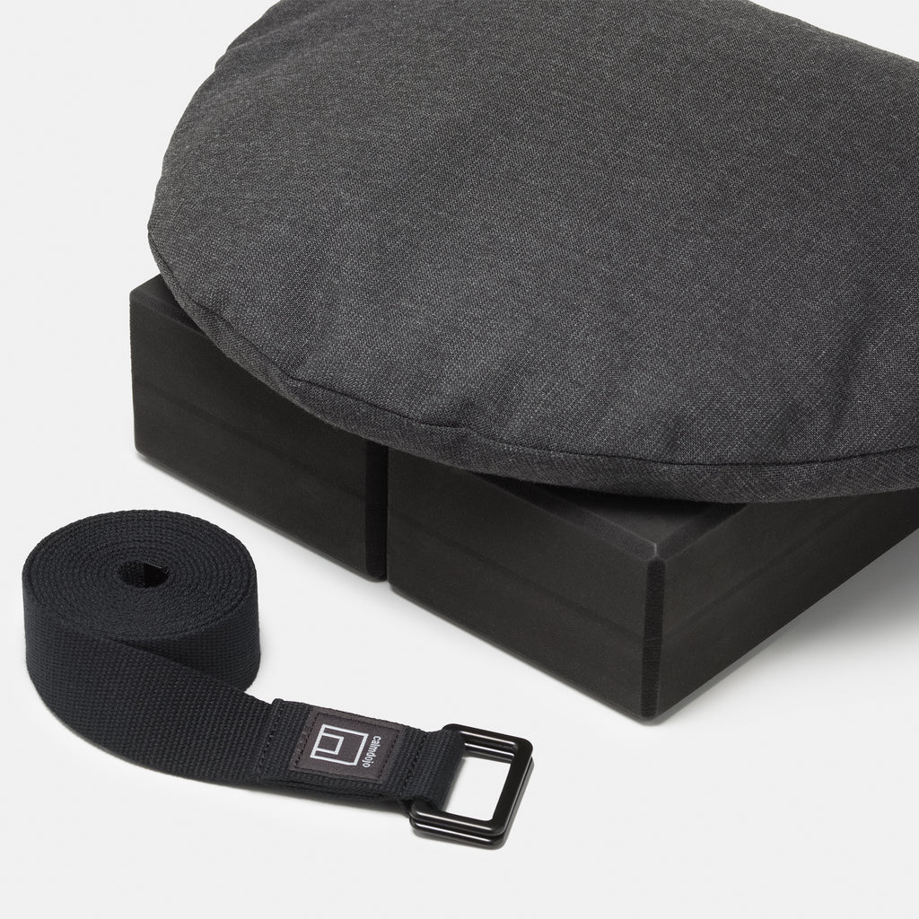 two black yoga blocks with triangular pillow on the top and black yoga strap int he forefront with calmdojo logo visible against a white background. 