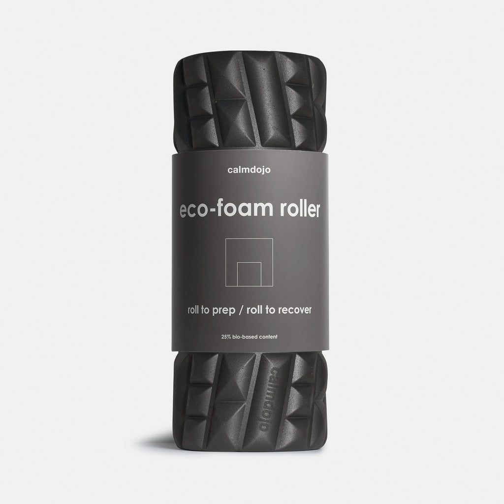 upright  black foam roller with gray belly band with laser engraved brand logo visible against a white background.