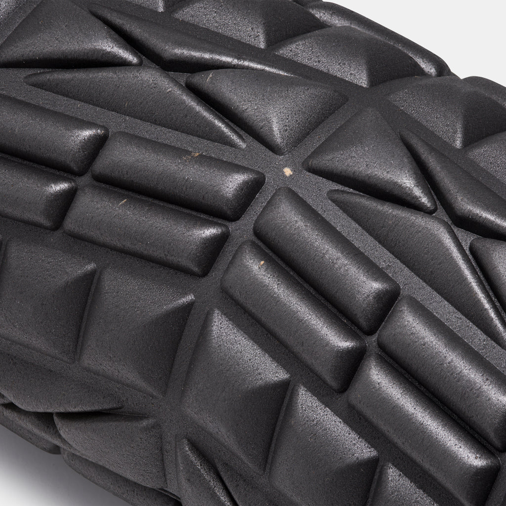 closeup of black foam roller with textured surface and flecks visible against a white background.