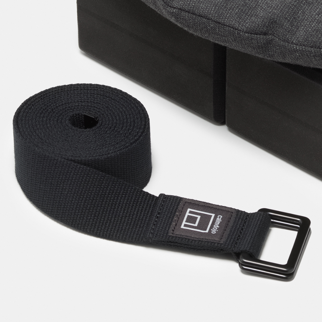 closeup of black yoga strap with yoga blocks and the edge of a gray pillow visible in the background.