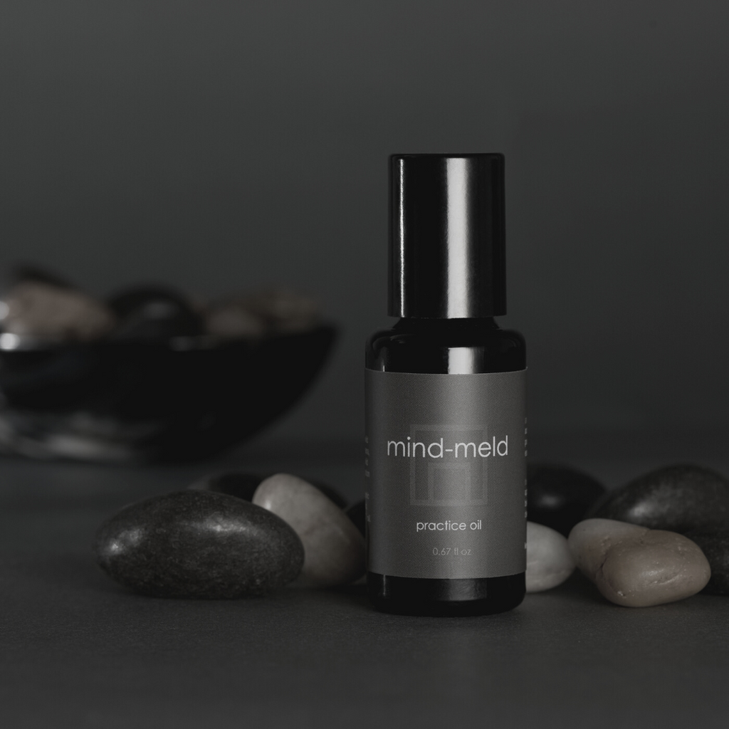 mind-meld practice oil product in a black glass bottle in a moody gray interior with stones and bowl in the background..