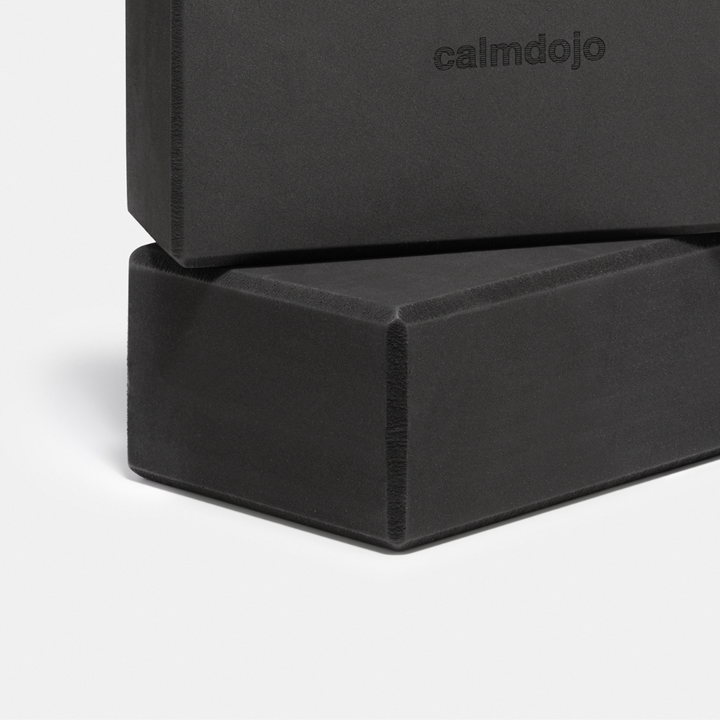 close up of two black yoga blocks stacked with the beveled edges visible.